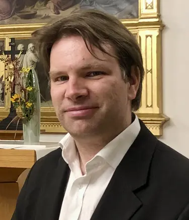 Kantor Jack Day mit schwarzem Jacket und weißem Hemd vor dem Altar der Luisenkirche. Braune Haare, Kurzhaarschnitt.