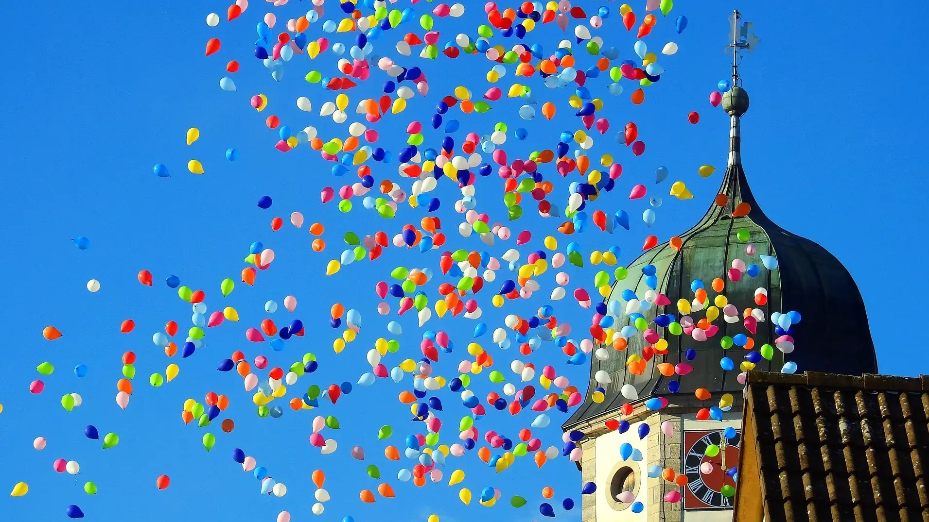 Aufsteigende bunte Luftballons vor einem Kirchturm