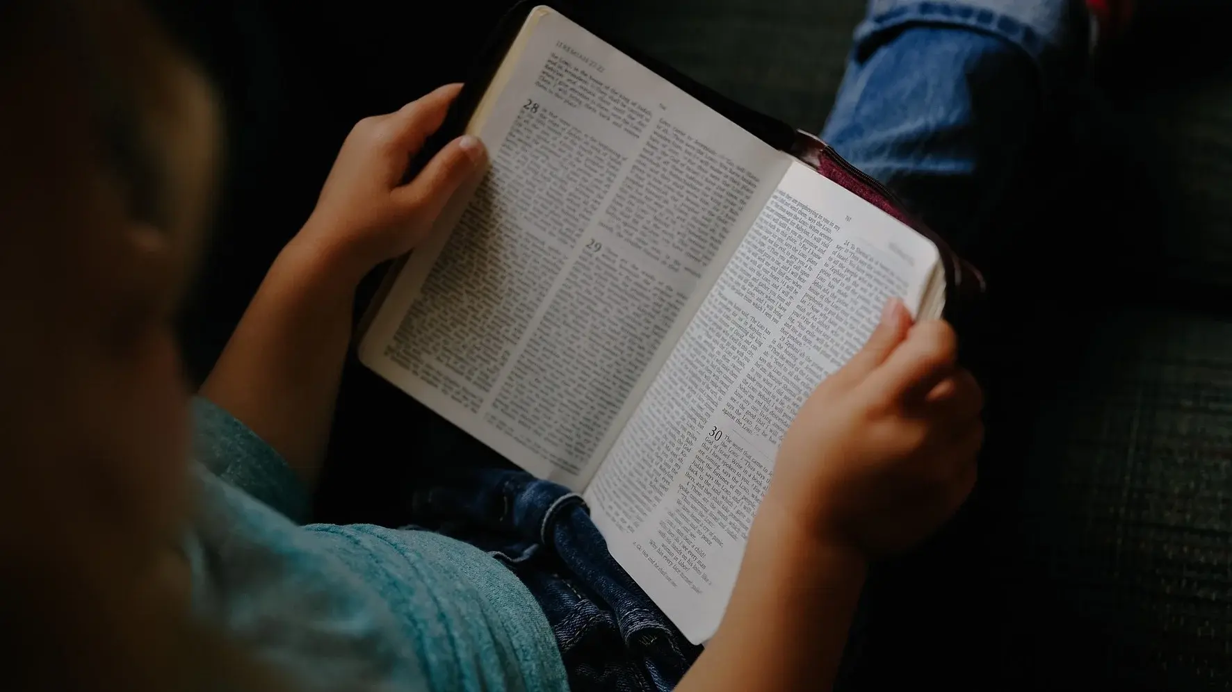 Sitzende Person, die eine aufgeschlagene Bibel in den Händen hält.